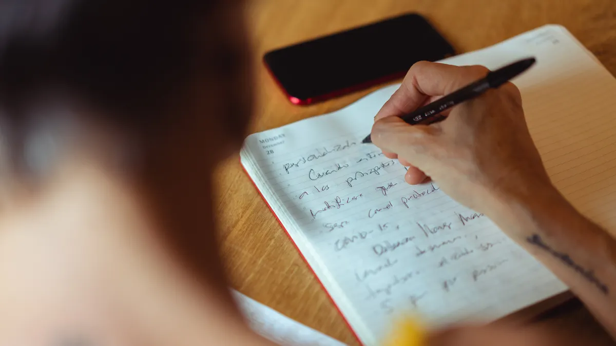Person journaling in an open notebook beside a phone