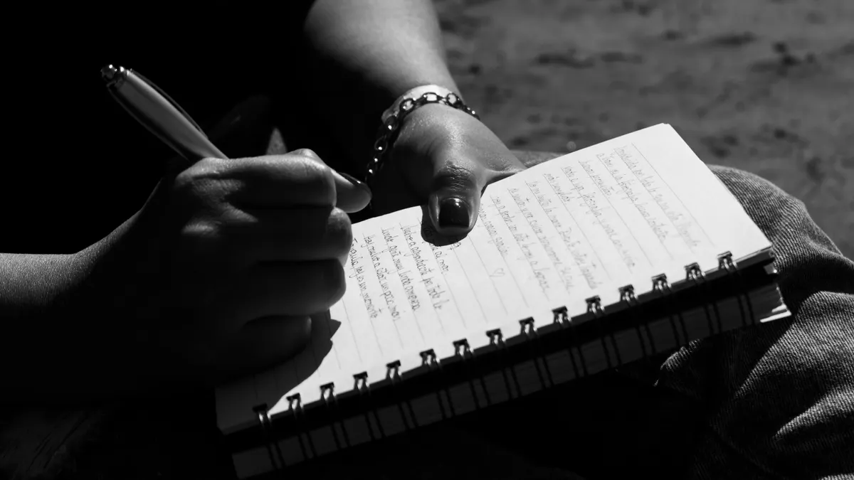 Close-up of hands writing in a spiral notebook