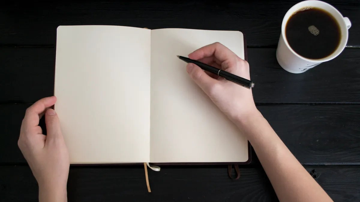hands writing in an open journal beside a coffee cup