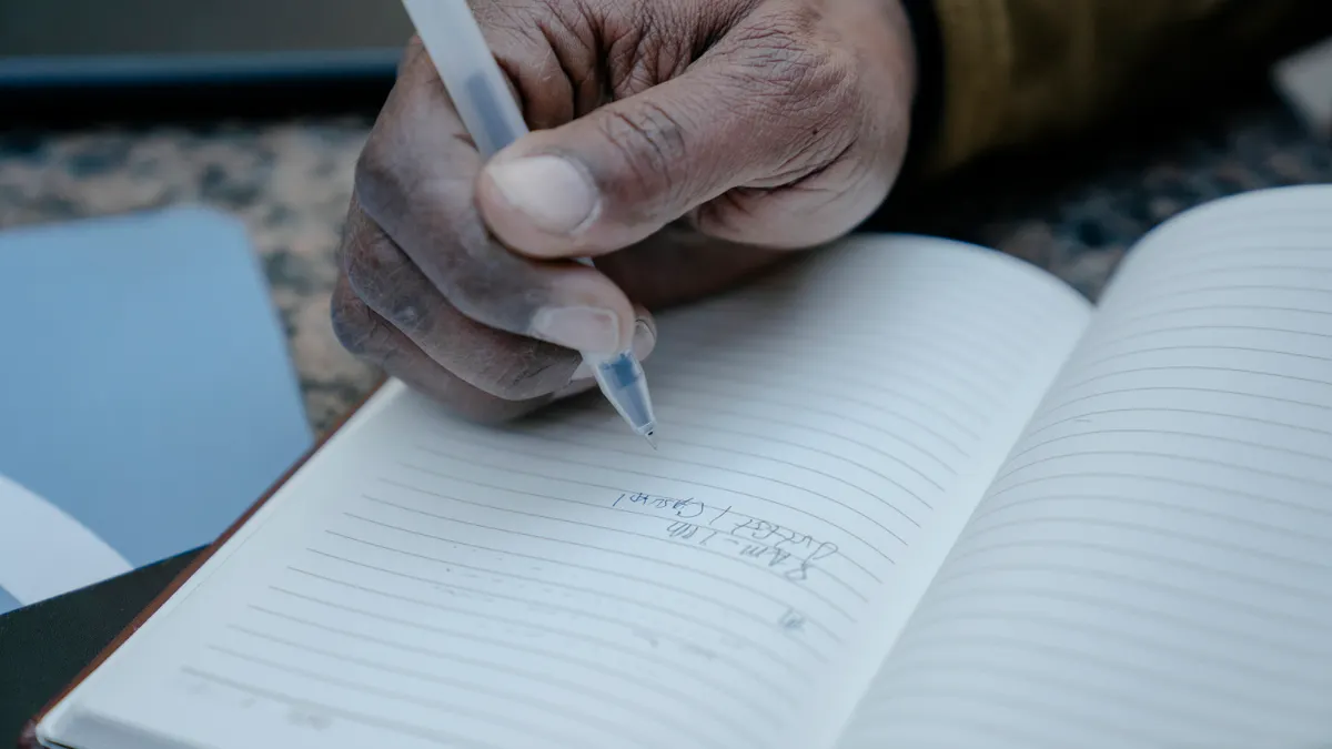 Close-up of a hand writing in a lined journal