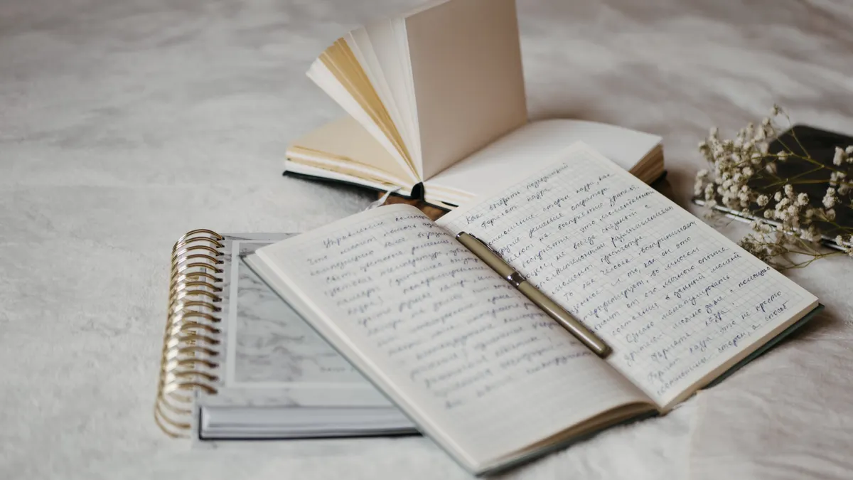 Handwritten journal pages with a pen and stacked notebooks