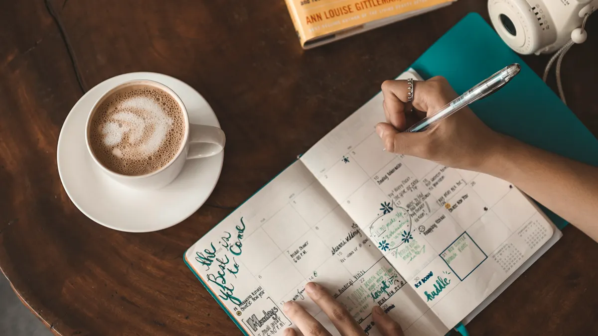 hands planning in a weekly journal next to coffee