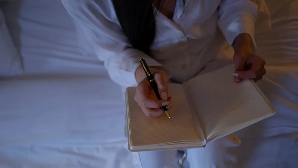 person journaling in an open notebook on a bed